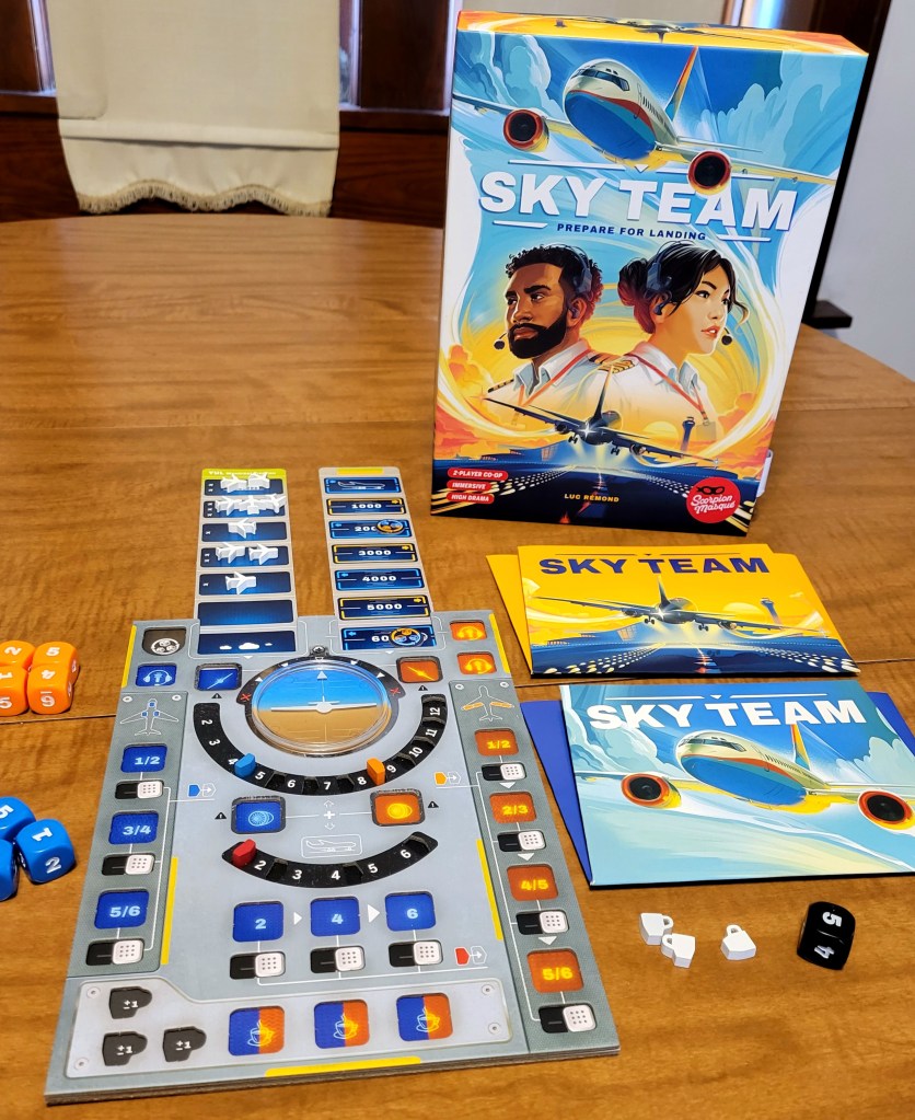 The board game "Sky Team" laid out on a table. The box is standing up and reads 'Sky Team - Prepare For Landing.' it has a picture of a plane in flight, two people with headsets, and a plane taking off. Directly below it there are two pieces of paper that say Sky Team, each with one of the planes from the box. To the lef is a complicate game board resembling an airplane's flight controls. On the table there are also two clusters of six sided dice in orange and blue, three coffee cup shaped pieces, and a single black six sided die.