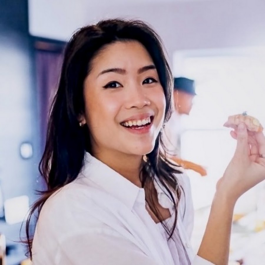 ID: An east Asian woman with long dark hair and light skin wearing a white shirt, holding a dumpling.