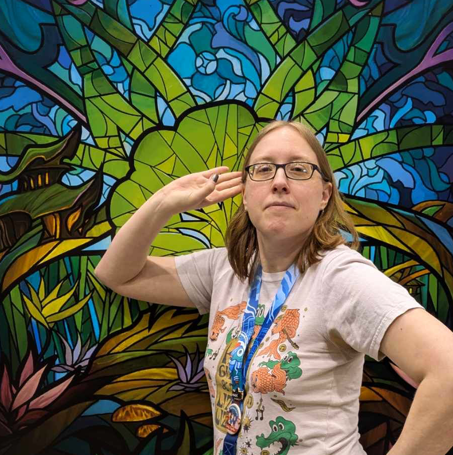 Photo of Hulyen posing in front of a stylized stained glass banner of a Forest mana symbol.