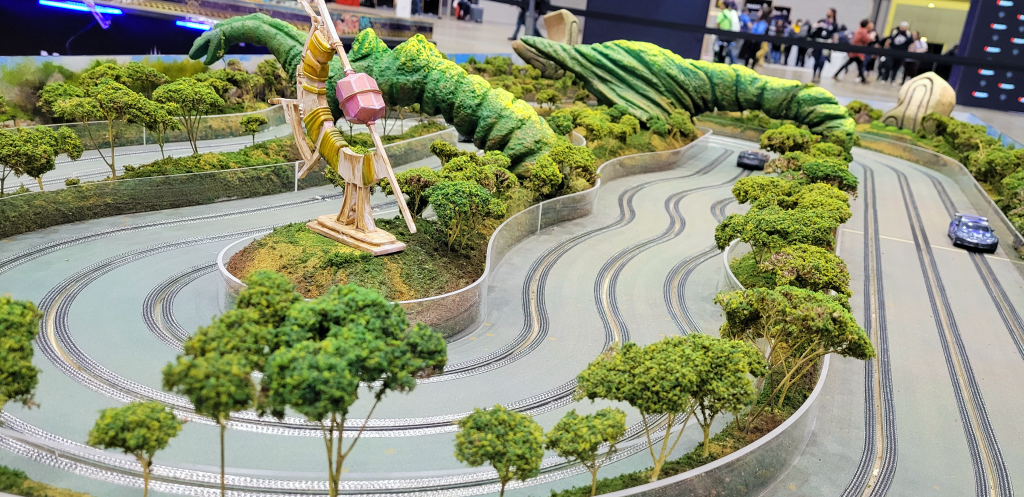 Closeup photo of slot cars racing through a jungled course with trees and large beasts.