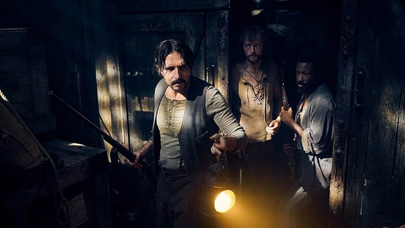 Image Description:
AS dark wooden cabein at night. Three sailors in late 18th century clothing are coming in from the door. They have guns and a lantern. They look concerned and frightened.
End Image Description.