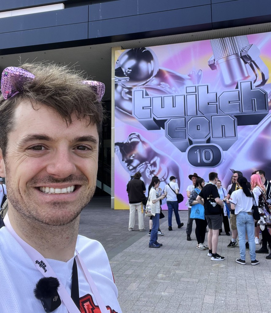 ID: Selfie of a smiling man with light skin and dark brown hair and eyes wearing a white t-shirt and pink, sequined kitty ears.  He is standing in front of a building with a large purple and silver sign that reads "twitch con 10."

Do you ever look at someone and think to yourself, "That is a bisexual man.  Not gay.  Specifically bisexual."  Well that is this picture.  